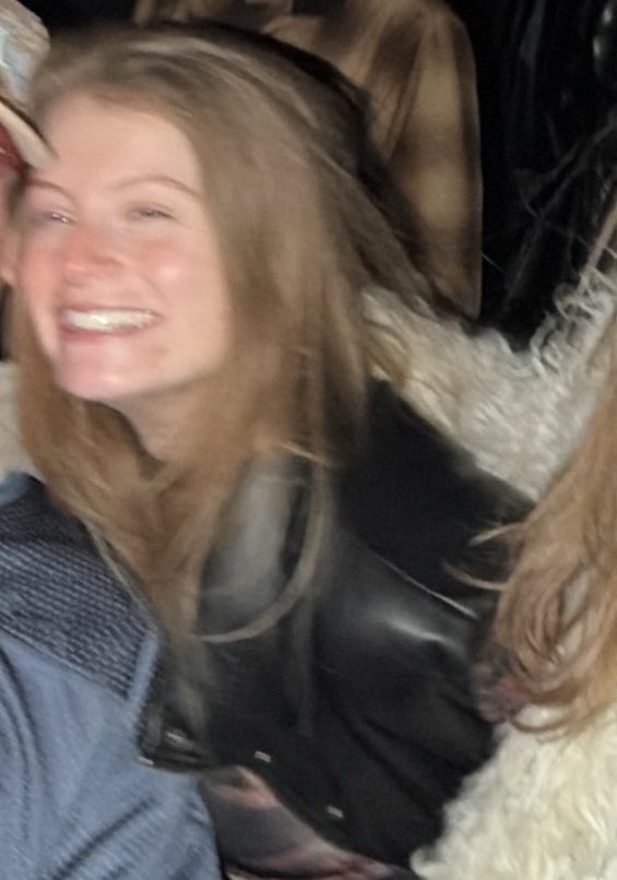 Dalia, blonde, in a leather jacket, laughing and slightly motion blurred.