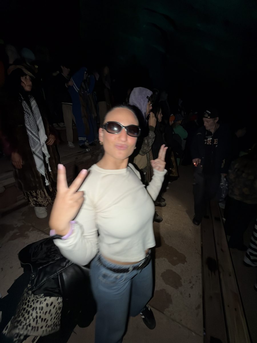 Jordy in a white top and sunglasses throwing two peace signs with a kissy face.
