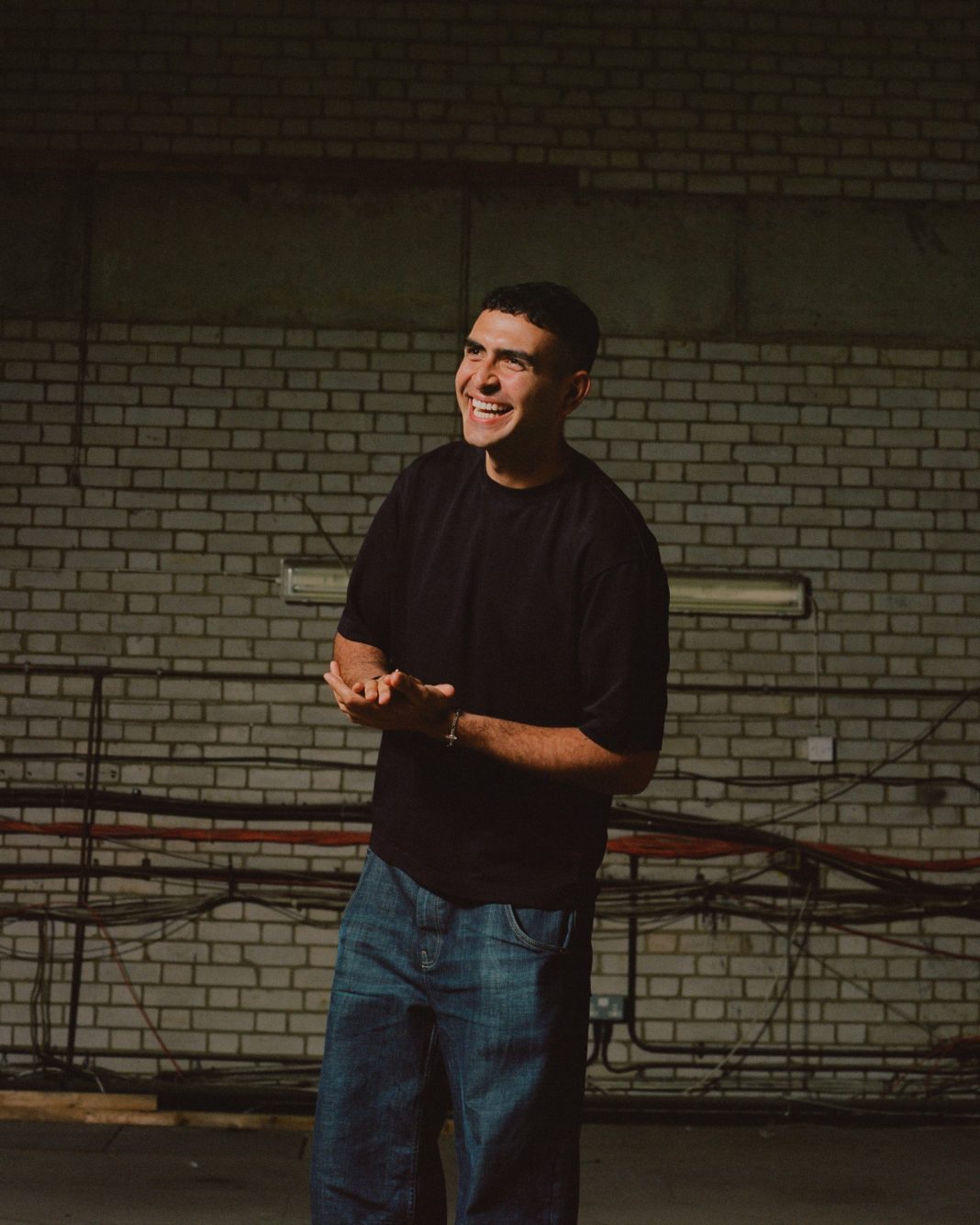 Sammy Virji smiling, standing in a dark warehouse.